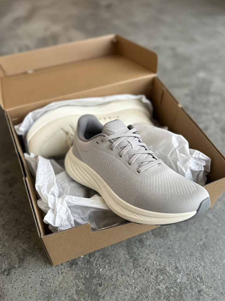Open kartonnen doos met grijze loopschoenen en kreukelpapier op beton
